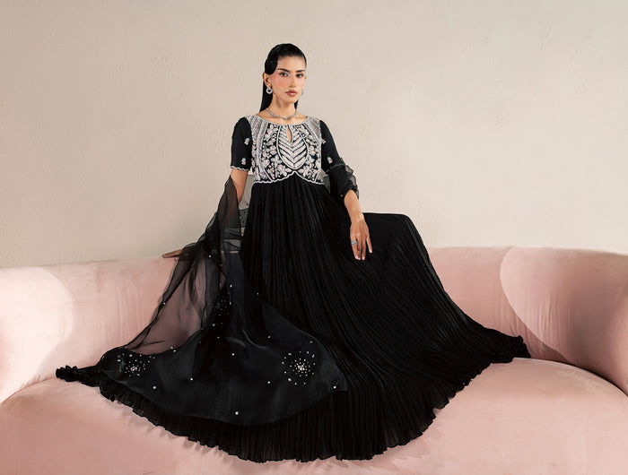 Model in Eraya Seréne black crushed silk peshwas with embellished yoke, seated on a pink velvet sofa